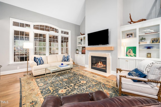 living room featuring baseboards, a fireplace with flush hearth, high vaulted ceiling, and wood finished floors