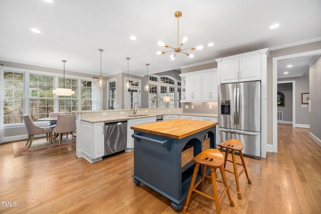 kitchen featuring a peninsula, a sink, appliances with stainless steel finishes, wood counters, and white cabinetry