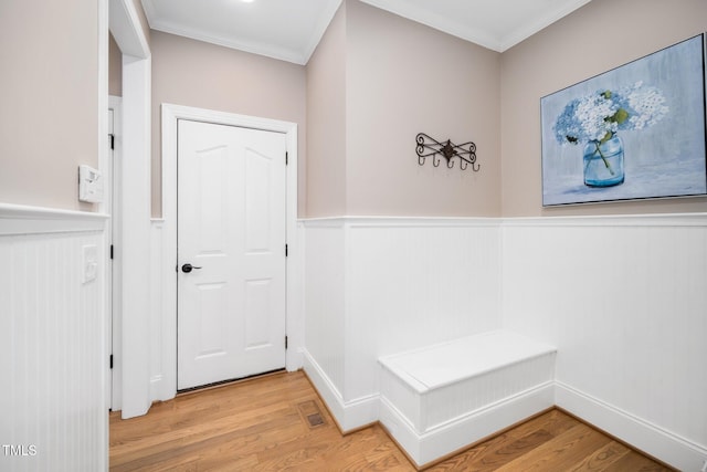 hall with a wainscoted wall, visible vents, crown molding, and light wood finished floors