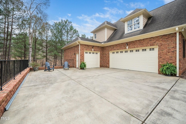 view of home's exterior featuring a shingled roof, brick siding, concrete driveway, and fence