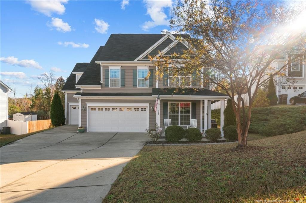 view of front of home featuring a porch, a garage, fence, driveway, and a front lawn