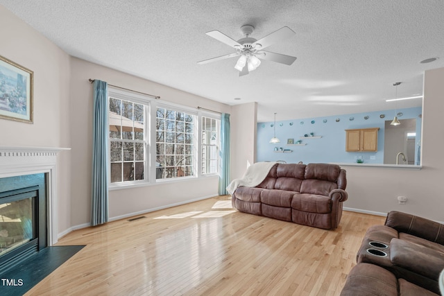 living area with a textured ceiling, a fireplace, visible vents, baseboards, and light wood-style floors