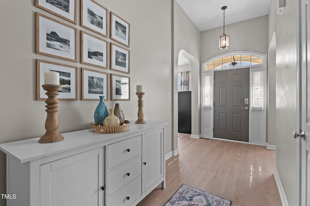 foyer entrance featuring arched walkways, light wood-type flooring, and baseboards