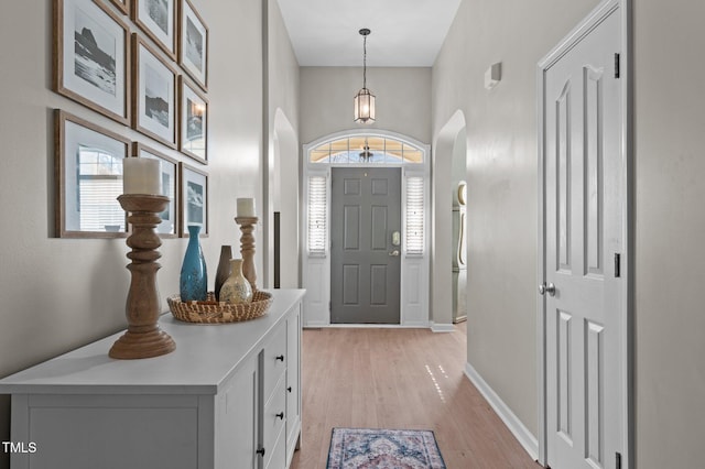 foyer entrance with arched walkways, light wood-type flooring, and baseboards