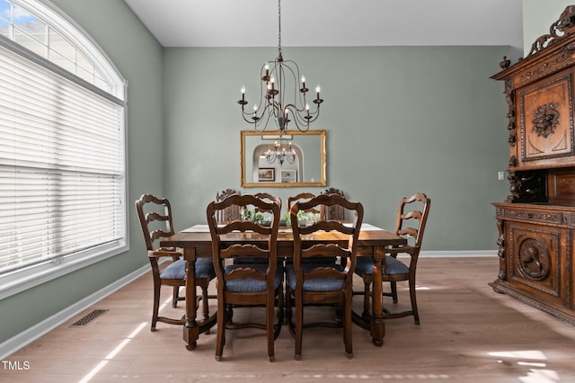 dining room with a healthy amount of sunlight, an inviting chandelier, light wood-style flooring, and visible vents