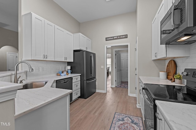 kitchen with appliances with stainless steel finishes, white cabinetry, a sink, light stone countertops, and light wood-type flooring