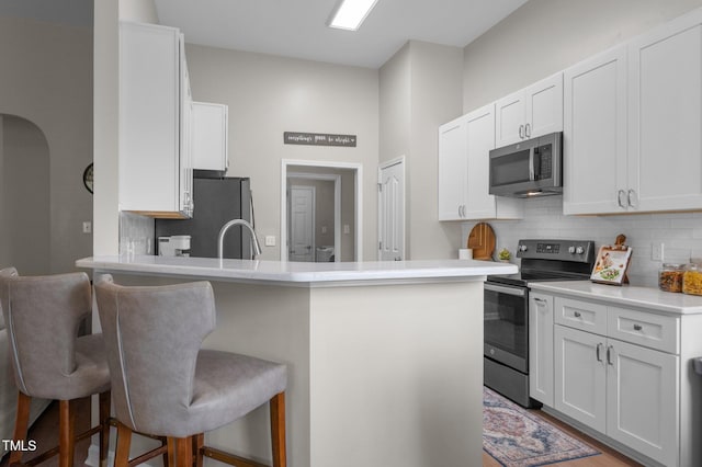 kitchen featuring tasteful backsplash, white cabinets, appliances with stainless steel finishes, a peninsula, and a kitchen bar