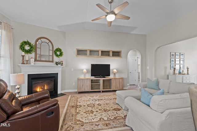 living room with arched walkways, baseboards, a ceiling fan, a fireplace with flush hearth, and wood finished floors