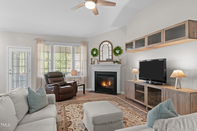 living room with baseboards, ceiling fan, a fireplace with flush hearth, wood finished floors, and vaulted ceiling