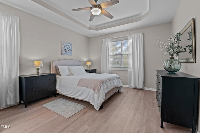 bedroom featuring a raised ceiling, light wood-style floors, ornamental molding, ceiling fan, and baseboards