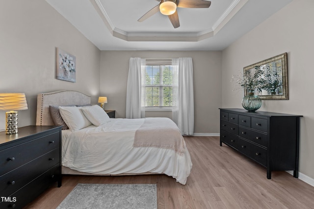 bedroom featuring ceiling fan, light wood-style flooring, baseboards, a raised ceiling, and crown molding