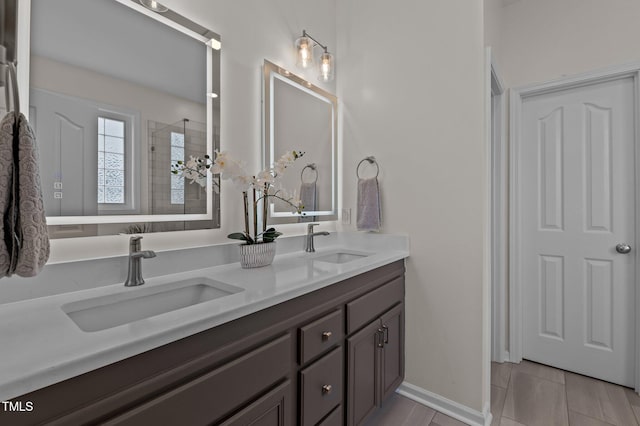 full bath featuring double vanity, tiled shower, a sink, and baseboards