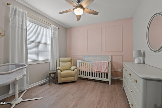 bedroom featuring visible vents, baseboards, ceiling fan, a nursery area, and light wood-style floors