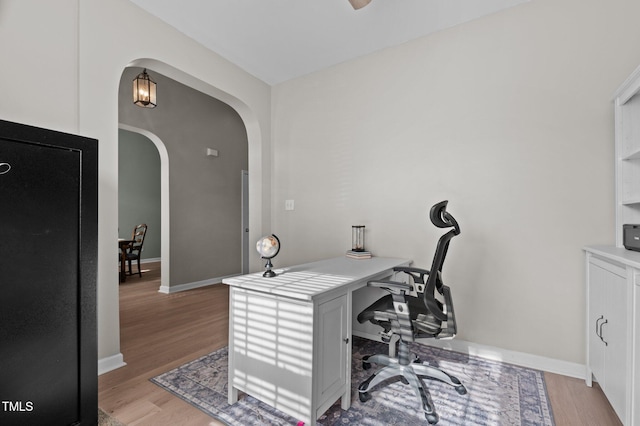 office space featuring arched walkways, baseboards, and light wood finished floors