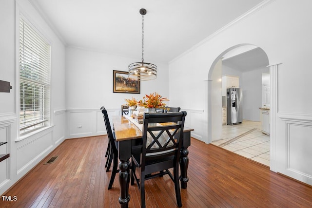 dining room featuring arched walkways, light wood-style flooring, visible vents, and crown molding