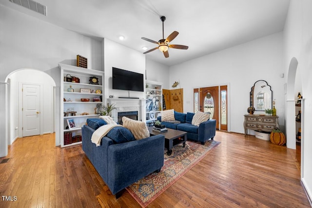 living room with visible vents, arched walkways, wood finished floors, a fireplace, and high vaulted ceiling