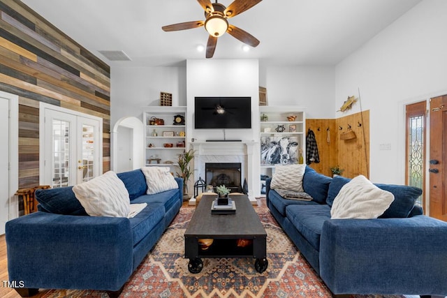 living area featuring arched walkways, wooden walls, a fireplace, visible vents, and french doors