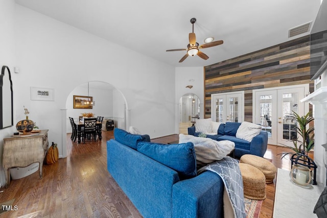 living room featuring wooden walls, visible vents, arched walkways, wood finished floors, and french doors