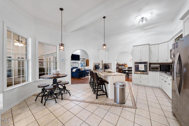 kitchen featuring arched walkways, light tile patterned floors, a kitchen breakfast bar, appliances with stainless steel finishes, and light stone countertops