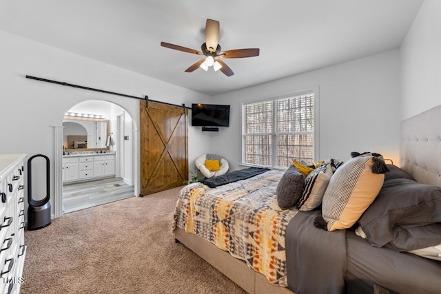 bedroom with arched walkways, light colored carpet, a barn door, a ceiling fan, and connected bathroom