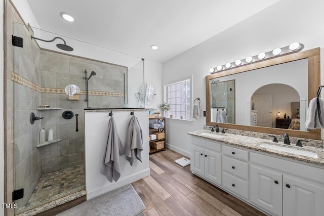 full bathroom featuring double vanity, tiled shower, wood finished floors, a sink, and recessed lighting