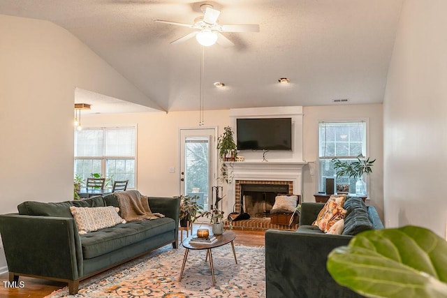 living room with lofted ceiling, a textured ceiling, a brick fireplace, and wood finished floors