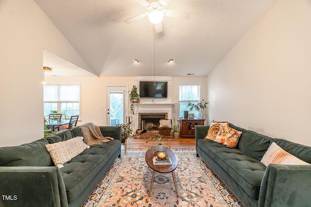 living room featuring a ceiling fan, lofted ceiling, a fireplace, and wood finished floors