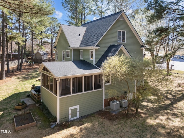 back of house featuring a vegetable garden, central air condition unit, a sunroom, and roof with shingles