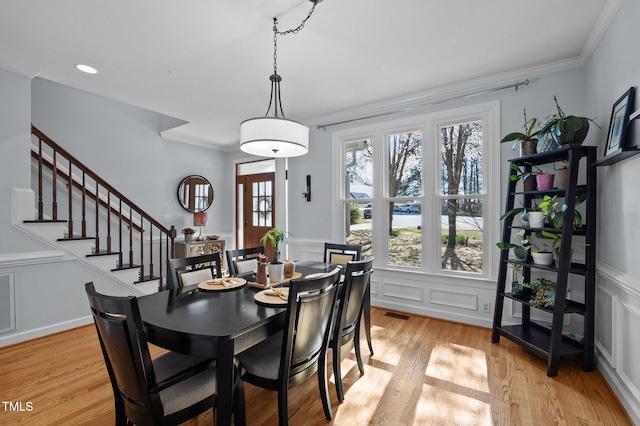 dining area featuring crown molding, stairway, light wood-style floors, and visible vents