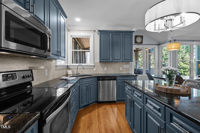 kitchen featuring light wood finished floors, blue cabinetry, a sink, stainless steel appliances, and backsplash