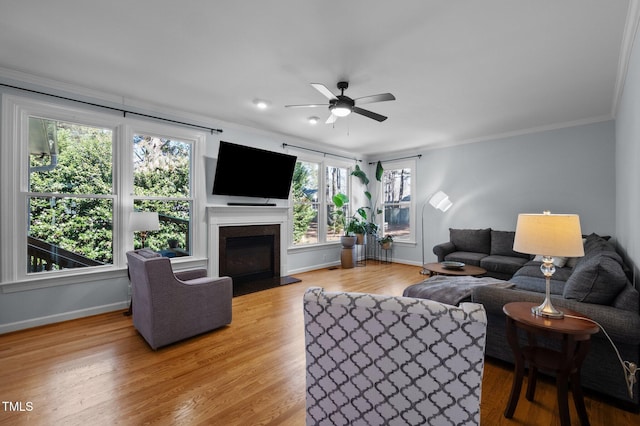 living room featuring light wood-style flooring, baseboards, a glass covered fireplace, and crown molding