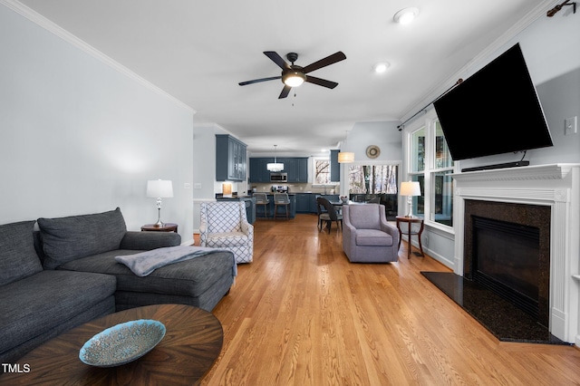 living room featuring a ceiling fan, baseboards, ornamental molding, light wood-style floors, and a glass covered fireplace