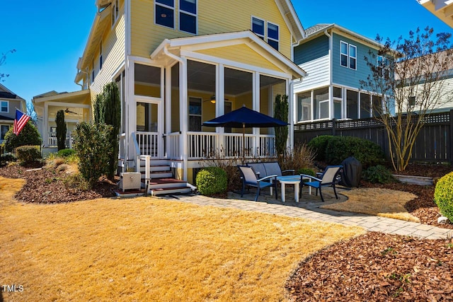 rear view of property with a lawn, an outdoor fire pit, a sunroom, a patio area, and fence