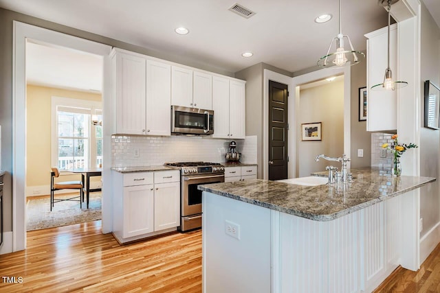 kitchen featuring light stone counters, stainless steel appliances, visible vents, light wood-style flooring, and a peninsula