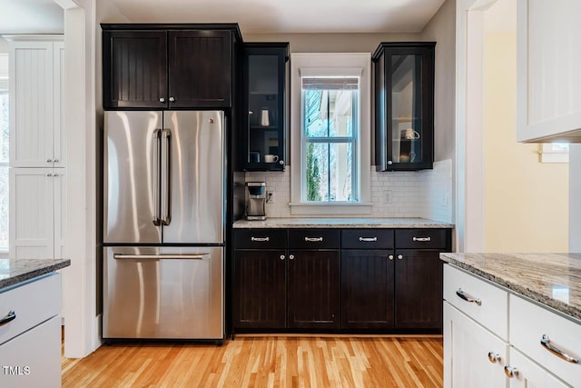 kitchen featuring light wood-style floors, tasteful backsplash, glass insert cabinets, and freestanding refrigerator