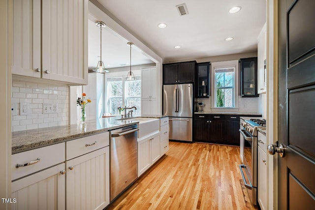 kitchen with light wood-style flooring, glass insert cabinets, appliances with stainless steel finishes, light stone counters, and a sink