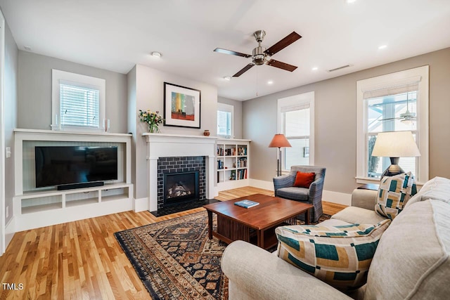 living room featuring a wealth of natural light, a tiled fireplace, visible vents, and wood finished floors