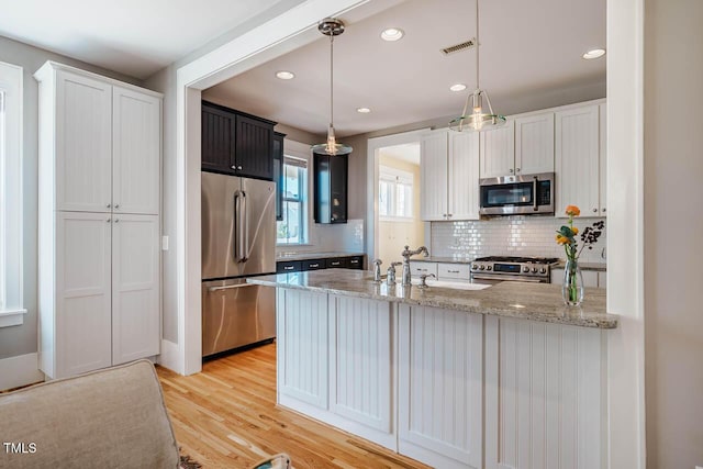 kitchen with visible vents, light wood-style flooring, appliances with stainless steel finishes, light stone counters, and a peninsula