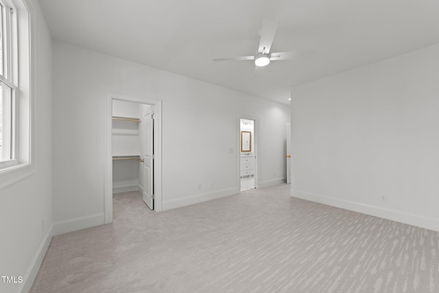 unfurnished bedroom featuring a walk in closet, a closet, ceiling fan, and baseboards