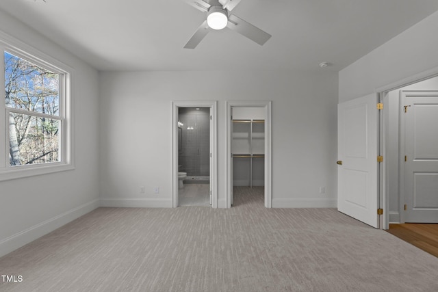 unfurnished bedroom with carpet floors, a spacious closet, ensuite bath, and baseboards