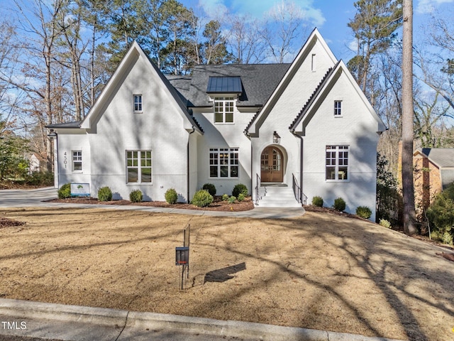 french country home featuring brick siding and roof mounted solar panels