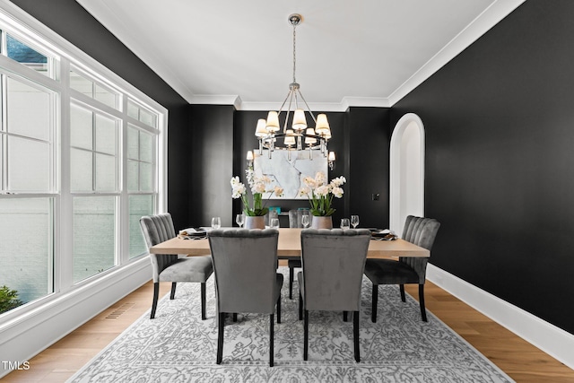 dining space featuring ornamental molding, arched walkways, baseboards, and light wood finished floors