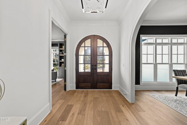 entryway with ornamental molding, arched walkways, french doors, and light wood finished floors