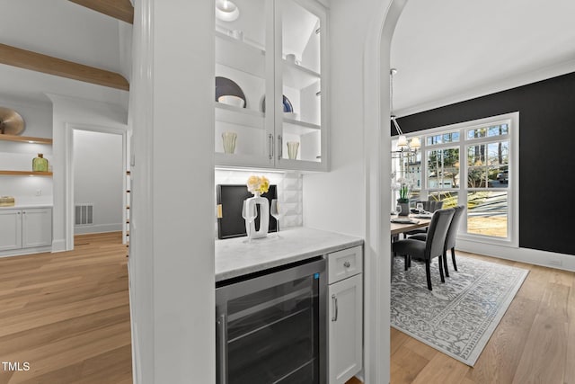 bar with wine cooler, a dry bar, visible vents, light wood-style flooring, and baseboards