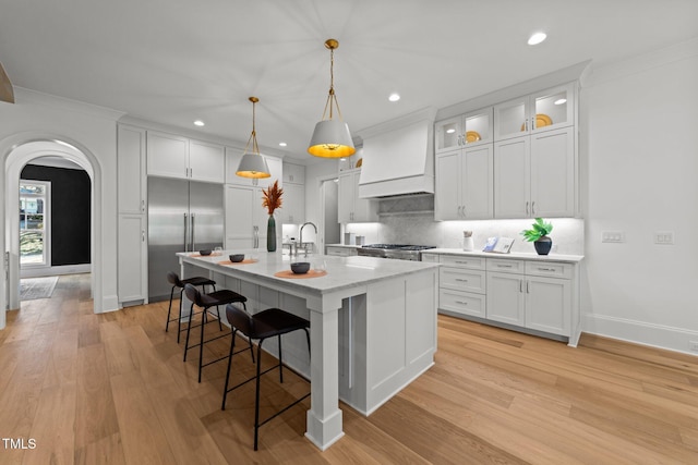 kitchen featuring arched walkways, white cabinets, custom exhaust hood, backsplash, and stainless steel built in refrigerator