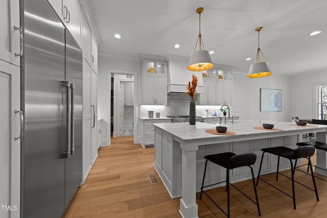 kitchen featuring light stone counters, built in refrigerator, light wood-type flooring, decorative backsplash, and custom range hood