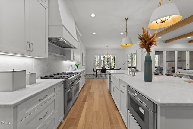 kitchen with custom exhaust hood, light wood finished floors, stainless steel appliances, backsplash, and light stone countertops