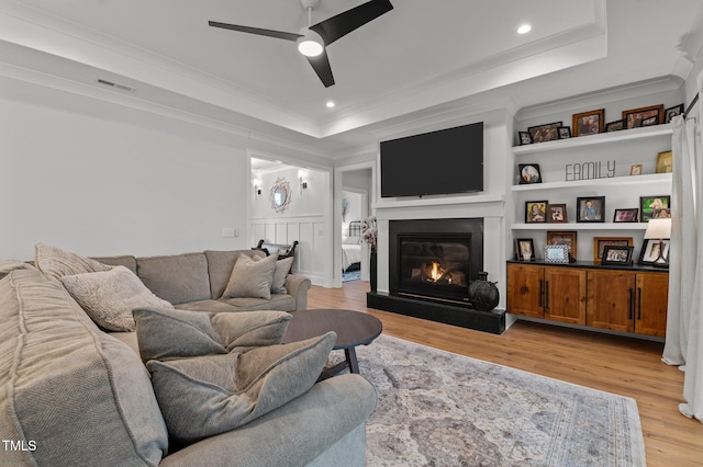 112 Rawhide Dr, Louisburg, NC 27549 - living area featuring a ceiling fan, light wood finished floors, a raised ceiling, a glass covered fireplace, and ornamental molding