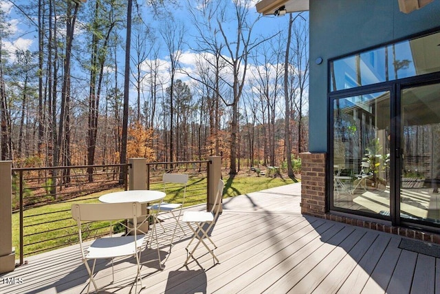 wooden terrace featuring a lawn and a wooded view