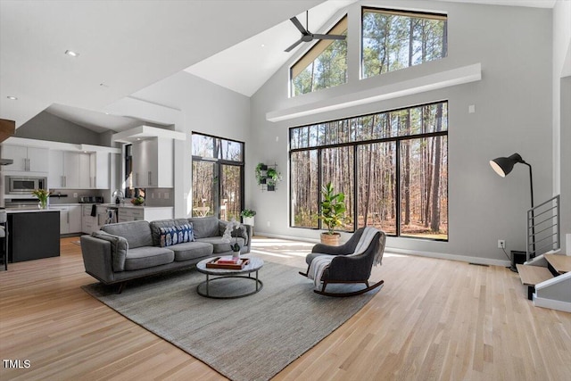 living area featuring light wood finished floors, high vaulted ceiling, baseboards, and ceiling fan